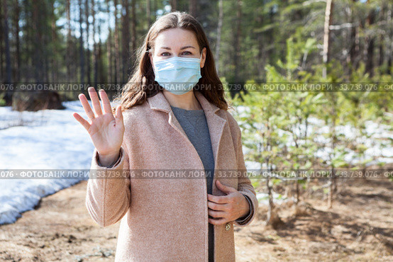 Young European woman waving with her hand while standing spring park wearing face mask, an allergy or virus prevention. Стоковое фото, фотограф Кекяляйнен Андрей / Фотобанк Лори