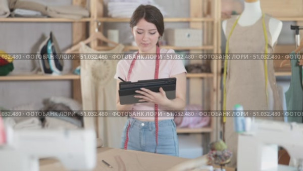 Young female seamstress draws pattern using tablet in sewing workshop. Стоковое видео, видеограф Яков Филимонов / Фотобанк Лори