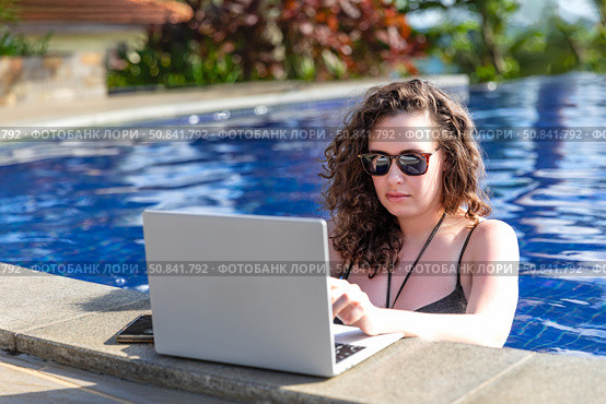 Young freelancer traveler woman working remotely on computer at pool in luxury resort during her summer holiday. Work from anywhere, Technology and lifestyle concept, copy space. High quality photo. Стоковое фото, фотограф Ирина Михайличенко / Фотобанк Лори