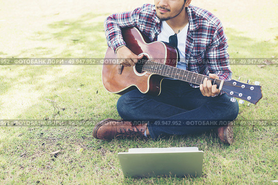 Young hipster man practiced guitar with laptop in the park,happy. Young hipster man practiced guitar with laptop in the park,happy and enjoy playing guitar. Стоковое фото, агентство Ingram Publishing / Фотобанк Лори