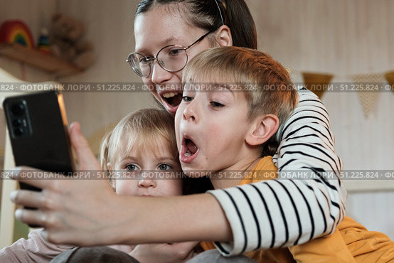 Young Kids Taking a Selfie Photo Together Using Smartphone During Fun Birthday Party in Decorated Room, Copy space. Family Moment. Selfie of Sisters and Brother, Small Children. Happy Childhood. Стоковое фото, фотограф Марина Демидюк / Фотобанк Лори