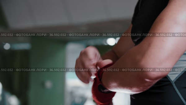 Young man boxer binds his palm and fingers with red bandages and stands in a protective stance. Стоковое видео, видеограф Константин Шишкин / Фотобанк Лори