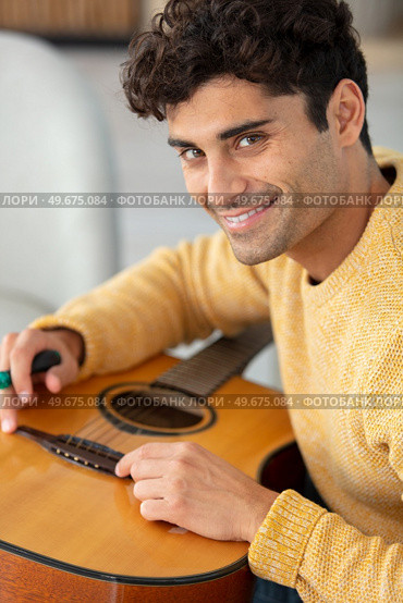 young man changing guitar strings at home. Стоковое фото, агентство Ingram Publishing / Фотобанк Лори