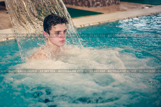 Young man having fun with the water in the swimming pool. Happy young man having fun and relaxing under a water jet at swimming pool. Стоковое фото, фотограф Evgenii Mitroshin / Фотобанк Лори