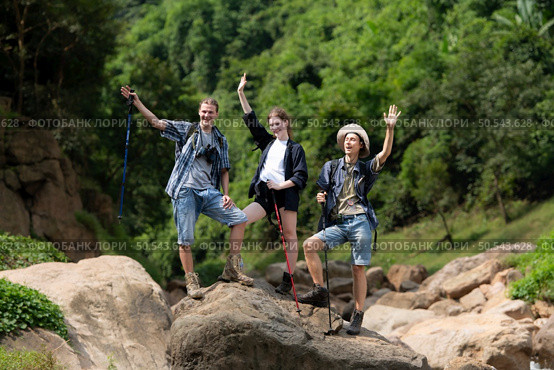 Young man hiker with backpack and trekking poles with a young man helping to pull him up to stand on the rock. Стоковое фото, агентство Ingram Publishing / Фотобанк Лори