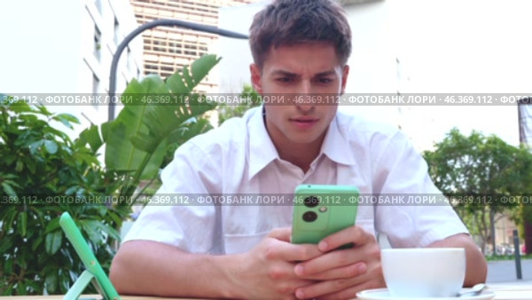 Young man in cafe looking at phone and shaking head in disapproval. Стоковое видео, видеограф Raquel Corcoles Mendez / Фотобанк Лори