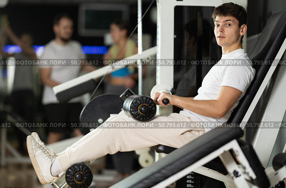 Young man in gym performs exercises for leg muscles using simulators and fitness center equipment. Стоковое фото, фотограф Яков Филимонов / Фотобанк Лори