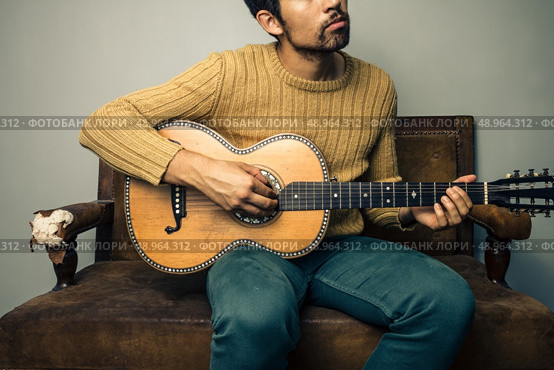 Young man playing guitar on sofa. Стоковое фото, агентство Ingram Publishing / Фотобанк Лори