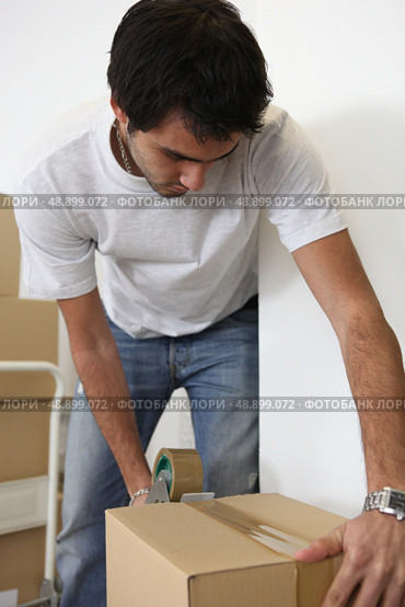 Young man taping shut a cardboard box. Стоковое фото, агентство Ingram Publishing / Фотобанк Лори