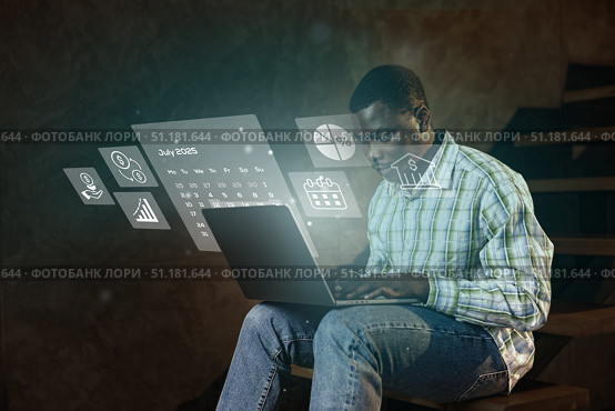 Young man using laptop while interacting with digital projections of charts and calendars in a cozy indoor setting. Стоковое фото, фотограф Сергей Толмачёв / Фотобанк Лори
