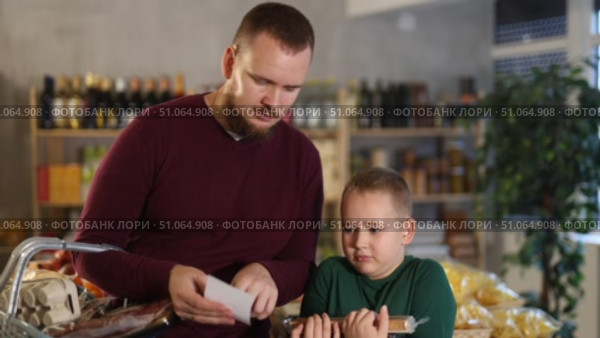 Young man with his son buying groceries from shopping list at grocery store. Стоковое видео, видеограф Яков Филимонов / Фотобанк Лори