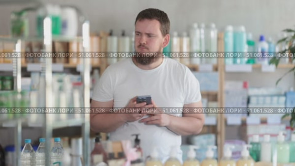 Young man with mobile phone choosing medicines and hygiene products in pharmacy. Стоковое видео, видеограф Яков Филимонов / Фотобанк Лори