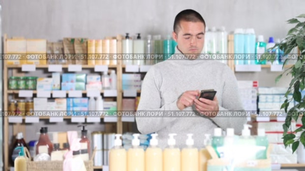 Young man with mobile phone choosing medicines and hygiene products in pharmacy. Стоковое видео, видеограф Яков Филимонов / Фотобанк Лори