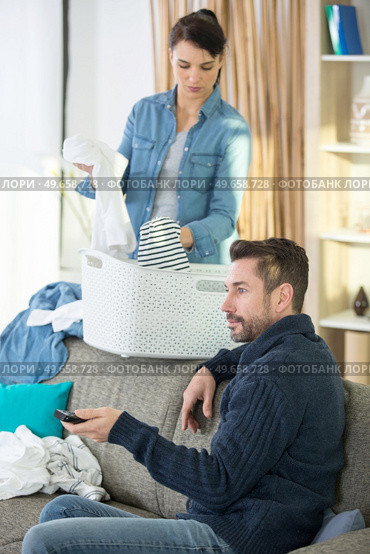 young woman doing laundry with boyfriend watching tv. Стоковое фото, агентство Ingram Publishing / Фотобанк Лори