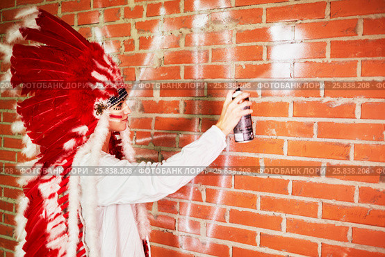 Young woman dressed in costume made of red and white feathers paints on the brick wall with spray. Стоковое фото, фотограф Losevsky Pavel / Фотобанк Лори