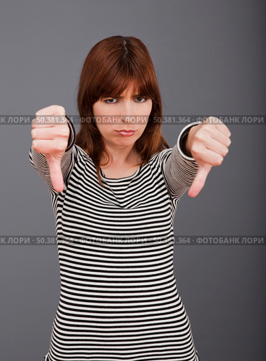 Young woman expressing negativity with thumb down over a grey background. Стоковое фото, агентство Ingram Publishing / Фотобанк Лори