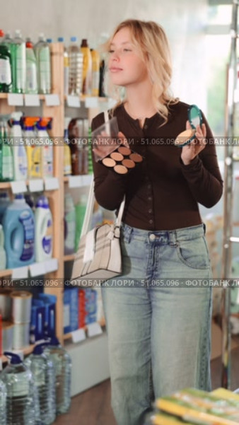 Young woman housewife in cosmetic store examines goods, chooses facial powder. Customer reads label and examines face makeup product. Buyer is shopping in household department. Стоковое видео, видеограф Яков Филимонов / Фотобанк Лори