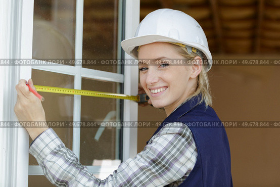 young woman measuring window with tape measurer. Стоковое фото, агентство Ingram Publishing / Фотобанк Лори