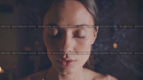 Young woman meditating with closed eyes in a dimly lit room, enveloped in swirling incense smoke, fostering a serene and tranquil ambiance that enhances her spiritual practice. Стоковое AI-видео, аниматор Данил Руденко / Фотобанк Лори