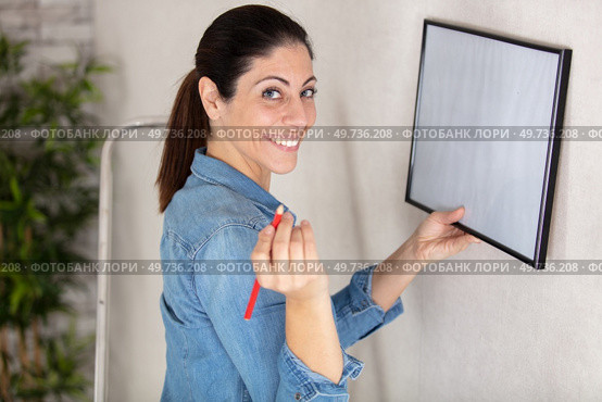 young woman putting photo frame on white wall. Стоковое фото, агентство Ingram Publishing / Фотобанк Лори