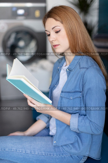 young woman reading a book in laundromat. Стоковое фото, агентство Ingram Publishing / Фотобанк Лори