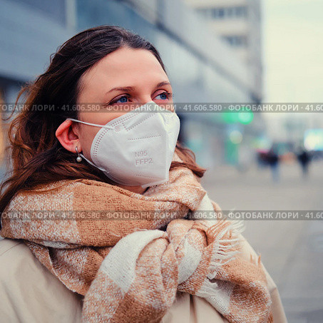 Young woman with curly hair in face mask with ffp2 respirator on a city street, outdoor. Стоковое фото, фотограф Андрей Журавлев / Фотобанк Лори
