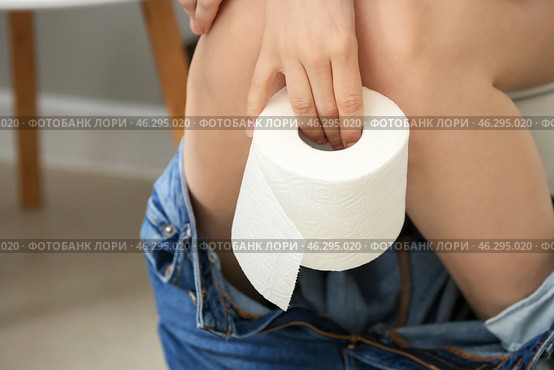Young woman with soft paper sitting on toilet bowl in restroom. Стоковое фото, фотограф Pixel_shot / Фотобанк Лори