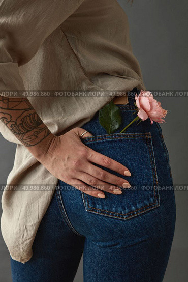 Young woman with tatoo hand and pink rose media in her pocket. View from the back. Against a gray background. Mother’s Day, Valentine’s Day. Woman with pink rose media in her pocket. Стоковое фото, агентство Ingram Publishing / Фотобанк Лори