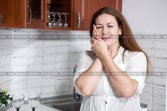 Young woman with toothache standing in kitchen, holding her cheek with hands. Стоковое фото, фотограф Кекяляйнен Андрей / Фотобанк Лори