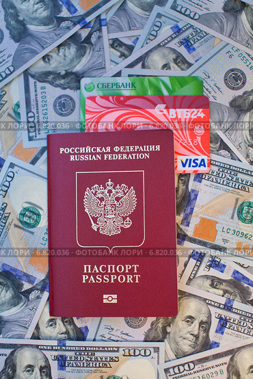 Заграничный паспорт гражданина Российской Федерации с вложенными банковскими картами на фоне 100-долларовых купюр (2014 год). Редакционное фото, фотограф Александр Тарасенков / Фотобанк Лори