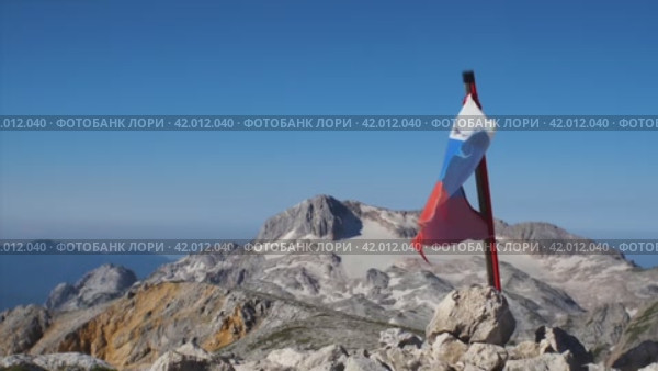 Замедленная съемка рваного российского флага, развивающегося на ветру. На заднем плане - голубое небо и заснеженные горы. Концепция горного туризма. Стоковое видео, видеограф Воловодов Владимир / Фотобанк Лори