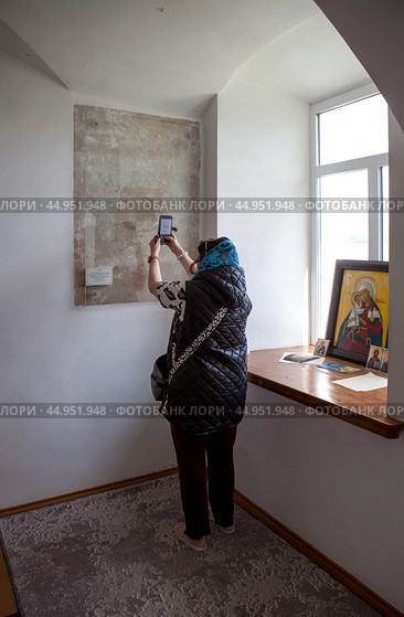 Женщина фотографирует нерукотворный Образ Спасителя на стене монашеской кельи Пустынского Свято-Успенского мужского монастыря. Мстиславский район. Могилевская область. Беларусь (2024 год). Редакционное фото, фотограф Сергей Афанасьев / Фотобанк Лори