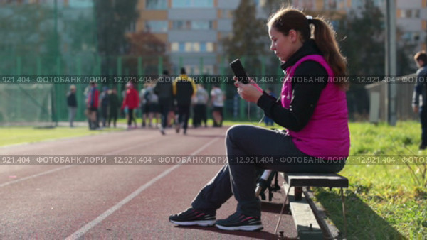 Женщина спортсменка делает селфи на телефон во время отдыха на скамейке на спортивном стадионе. Стоковое видео, видеограф Кекяляйнен Андрей / Фотобанк Лори