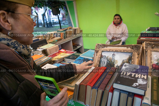 Женщина в пилотке выбирает старые книги в продаже на ретро-маркете в рамках фестиваля "Московская весна" на Никитском бульваре в центре города Москвы, Россия (2023 год). Редакционное фото, фотограф Николай Винокуров / Фотобанк Лори