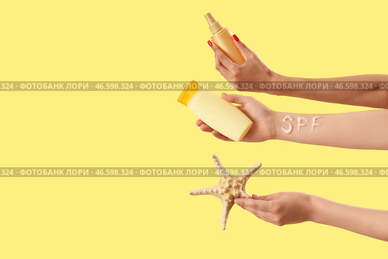 Женские руки с нанесенными буквами SPF, солнцезащитными кремами и морской звездой на желтом фоне. Стоковое фото, фотограф Pixel_shot / Фотобанк Лори
