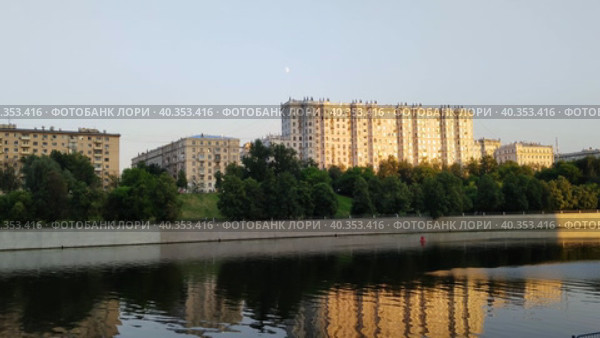 Жилой район на противоположном берегу широкой реки. Заходящее солнце освещает жилые здания. Спокойная городская река. Деревья и набережная отражаются на поверхности воды. Теплый вечер в большом городе. Residential area on the opposite bank of a wide river. Setting sun illuminates residential buildings. Calm city river. Trees and embankment are reflected on surface of water. Warm evening in big city. Стоковое видео, видеограф Ирина / Фотобанк Лори
